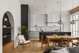 Salon z otwartą kuchnią, jodełkową podłogą dębową, czarnym łukowym przejściem do strefy z kominkiem i fotelem w stylu mid-century