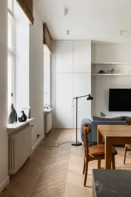 Salon z białą zabudową telewizyjną, czarną lampą podłogową w stylu industrialnym i widokiem na strefę jadalni