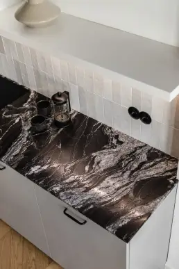 Zbliżenie na blat z czarnego granitu z białymi żyłkami, kafelkowym fartuchem i porcelanową kawiarką z dwiema filiżankami.