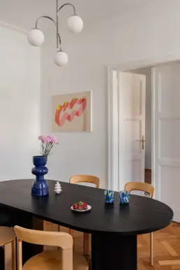 Detal jadalni z kobaltową ceramiczną wazą, kolorową grafiką na ścianie i drewnianymi drzwiami z mosiężną klamką.
