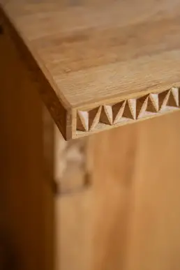 Zbliżenie na ręcznie snycerską krawędź dębowego mebla z geometrycznym, trójkątnym wzorem rzeźbionym w drewnie.