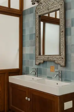 Strefa umywalkowa z podwójną ceramiczną umywalką na drewnianej szafce, marokańskim lustrem w srebrnej ramie i fartuchem z ręcznie wykonanych kafli zellige.