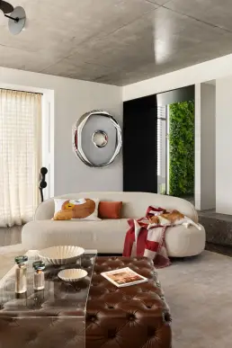 esignerska sofa boucle z dekoracyjnym lustrem ze stali nierdzewnej i ścianą zieleni w tle warszawskiego domu
