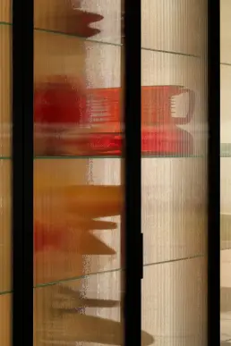 Detal ryflowanego szkła w czarnych ramach z widocznymi czerwonymi i pomarańczowymi refleksami w tle