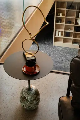 Designerski stolik pomocniczy z kamienną podstawą, ceramiczną filiżanką i mosiężną rzeźbą