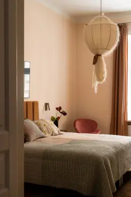 Sypialnia w odcieniach pudrowego różu i terakoty z welurowym karmelowym zagłówkiem, baldachimowym kloszem z gazy, narzutą w kratkę i różowym fotelem przy oknie.