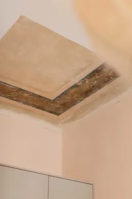 Zbliżenie na fragment oryginalnego polichromowanego sufitu z geometrycznym wzorem, odsłoniętego nad zabudową szafy w sypialni.