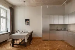 Otwarta strefa kuchenno-jadalniana ze stalową zabudową kuchenną, drewnianym stołem z giętymi krzesłami i odsłoniętym oryginalnym sufitem w stylu vintage.