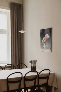 Kącik jadalny z drewnianymi krzesłami w stylu thonet, lnianym obrusem, ceramiczną rzeźbą i fotograficznym plakatem z papugą na ścianie