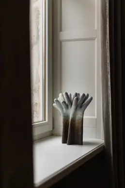 Ceramiczna rzeźba w kształcie splecionych dłoni w niebiesko-brązowej glazurze, ujęcie z bliska na parapecie