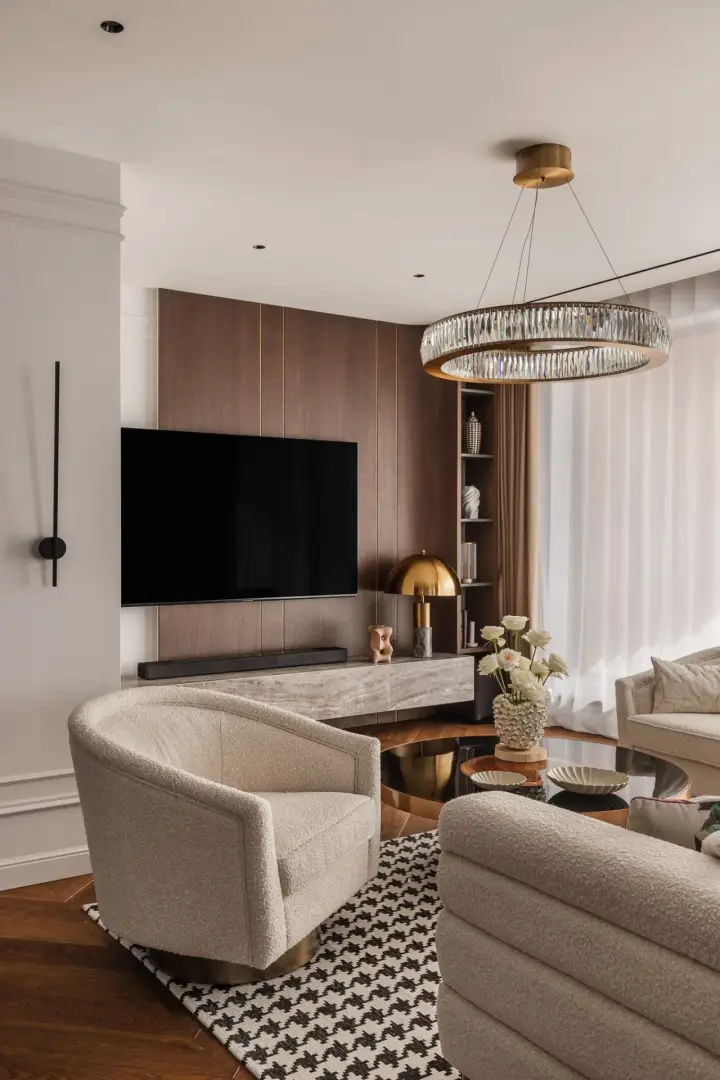 Zabudowa telewizyjna z forniru z mosiężnymi wstawkami i fotel bouclé – zdjęcia wnętrz luksusowego apartamentu
