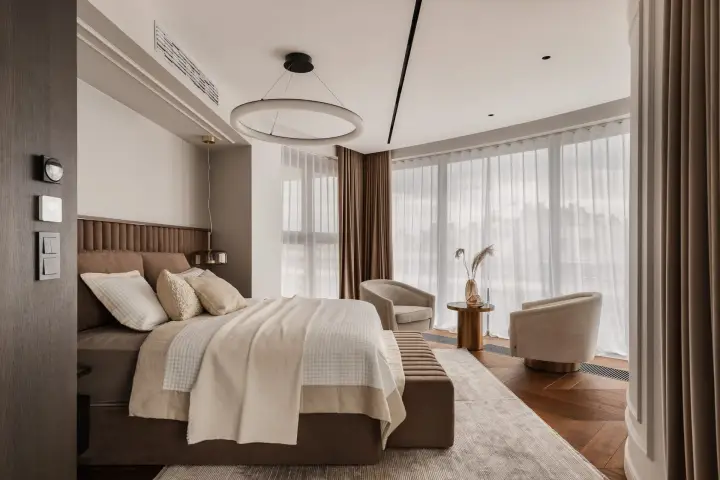 Sypialnia master z tapicerowanym zagłówkiem, fotelami i przeszkleniem na miasto – zdjęcia wnętrz luksusowego apartamentu