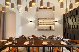 restauracja Muro Rzeszów — długi stół z nakryciami pod ceramicznymi lampami, regał na wino i ściana z drewnianych bloków