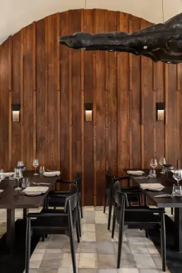 restauracja Muro Rzeszów — stoliki z czarnymi krzesłami przy łukowej ścianie z drewnianych desek i wbudowanymi kinkietami
