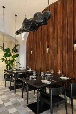 restauracja Muro Rzeszów — stoliki z czarnymi krzesłami przy drewnianej ścianie z kinkietami i rzeźbą nad głowami