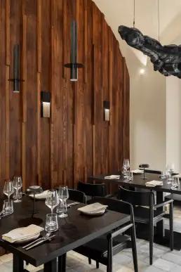 restauracja Muro Rzeszów — stolik widziany przez zasłonę przy ścianie z drewnianych lameli i rzeźbą pod sufitem