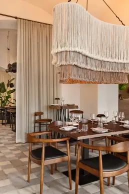 restauracja Muro Rzeszów — nakryty stół pod makramową lampą z frędzlami, lniane zasłony i stolik barowy z plastra drewna w tle
