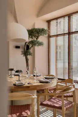 restauracja Muro Rzeszów — okrągły drewniany stół z plecionymi krzesłami przy drzewku oliwnym, białą kopułową lampą i cieniami żaluzji
