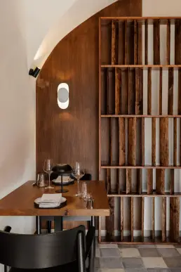 restauracja Muro Rzeszów — kameralny stolik w niszy z łukową orzechową ścianą, owalnym kinkietem i regałem z surowych belek