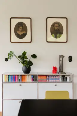 Komoda z kolorowymi książkami, zabytkowe portrety i monstera