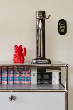 Detal komody z kolekcją książek o sztuce, figurką lucky cat i ekspresem