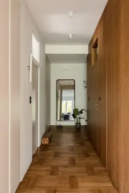 Korytarz z parkietem jodełkowym, dębową zabudową i lustrem pełnowymiarowym