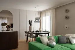 Otwarta przestrzeń łącząca salon z zieloną sofą modułową, jadalnię z czarnym stołem i aneks kuchenny z ciemnym fornirowanym frontem oraz arkadowym przejściem.