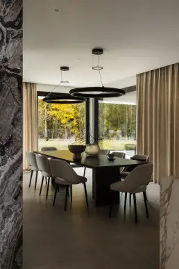 Jadalnia z widokiem na jesienny las przez panoramiczne okna i designerskimi lampami wiszącymi w formie pierścieni