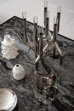 Detal kompozycji dekoracyjnej z chromowanym świecznikiem ze szklanymi tubami i ceramicznymi wazonami na marmurowym blacie
