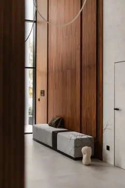 Dwukondygnacyjny hol wejściowy z wysoką ścianą boazerii z orzecha, szarą ławką tapicerowaną i designerską lampą wiszącą