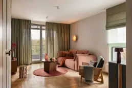 salon z sofą bouclé, okrągłym dywanem, oliwkowymi zasłonami i balkonem