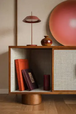 detal szafki RTV z książkami, bordową lampą i ceramicznym wazonem na tle paneli z tkaniny