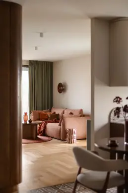 widok z kuchni na salon przez orzechową kolumnę z sofą i pasiastym pufem
